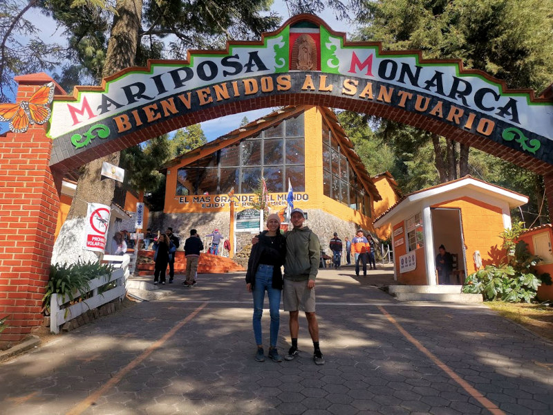 A couple standing under the entrance arch to El Rosario Butterfly Sanctuary