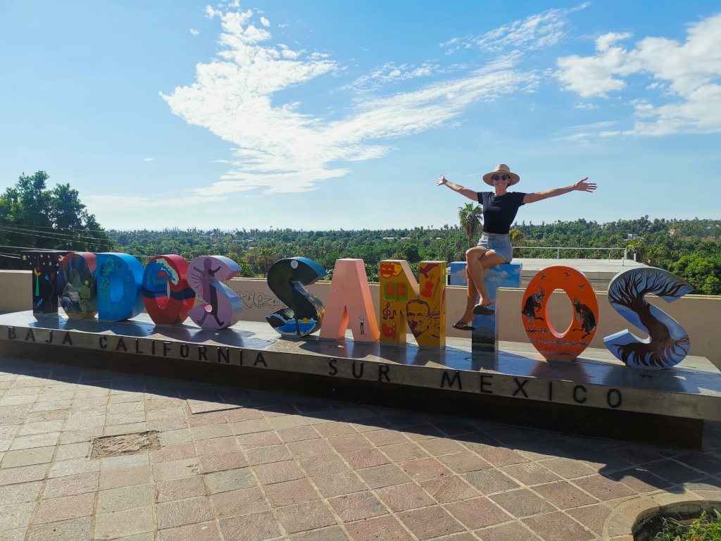 A woman sitting with her arms stretched out on top of some colorful letters in todos santos mexico