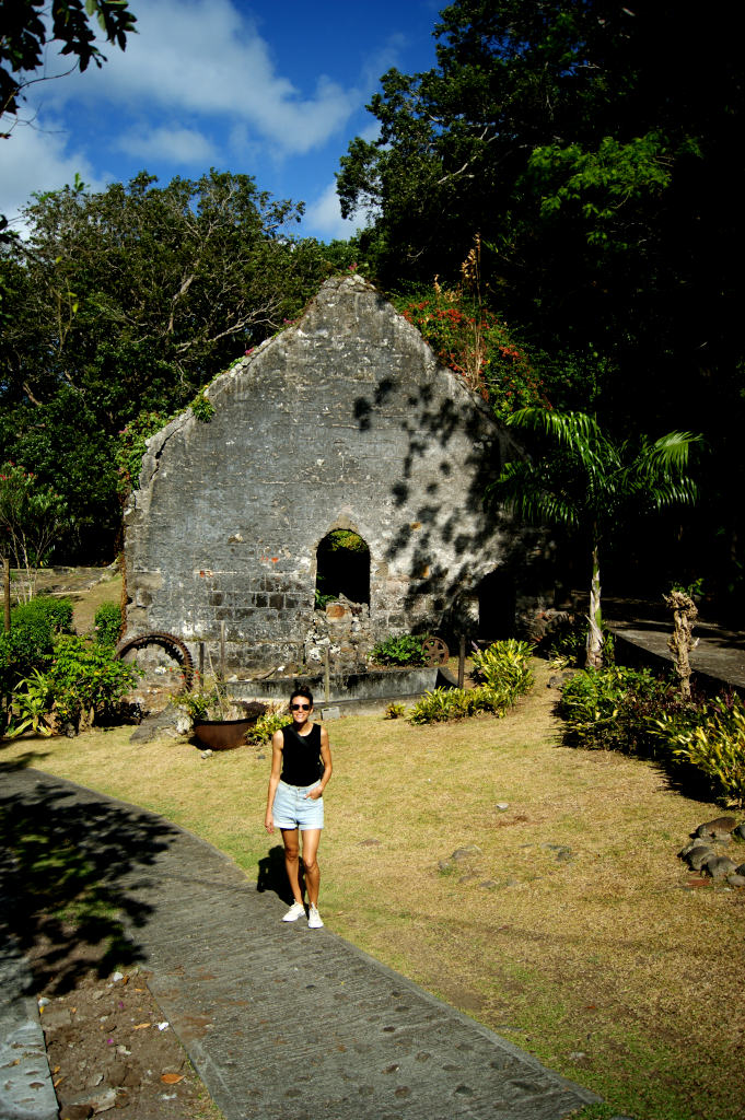 A woman in a black top and denim shirts standing in front of some ruins at Belmont Estate in Grenada
