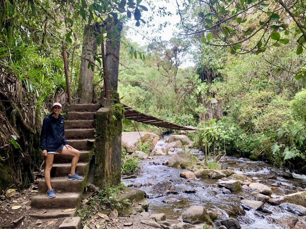 A woman posing in front of a staircase and a wooden bridge in a forest