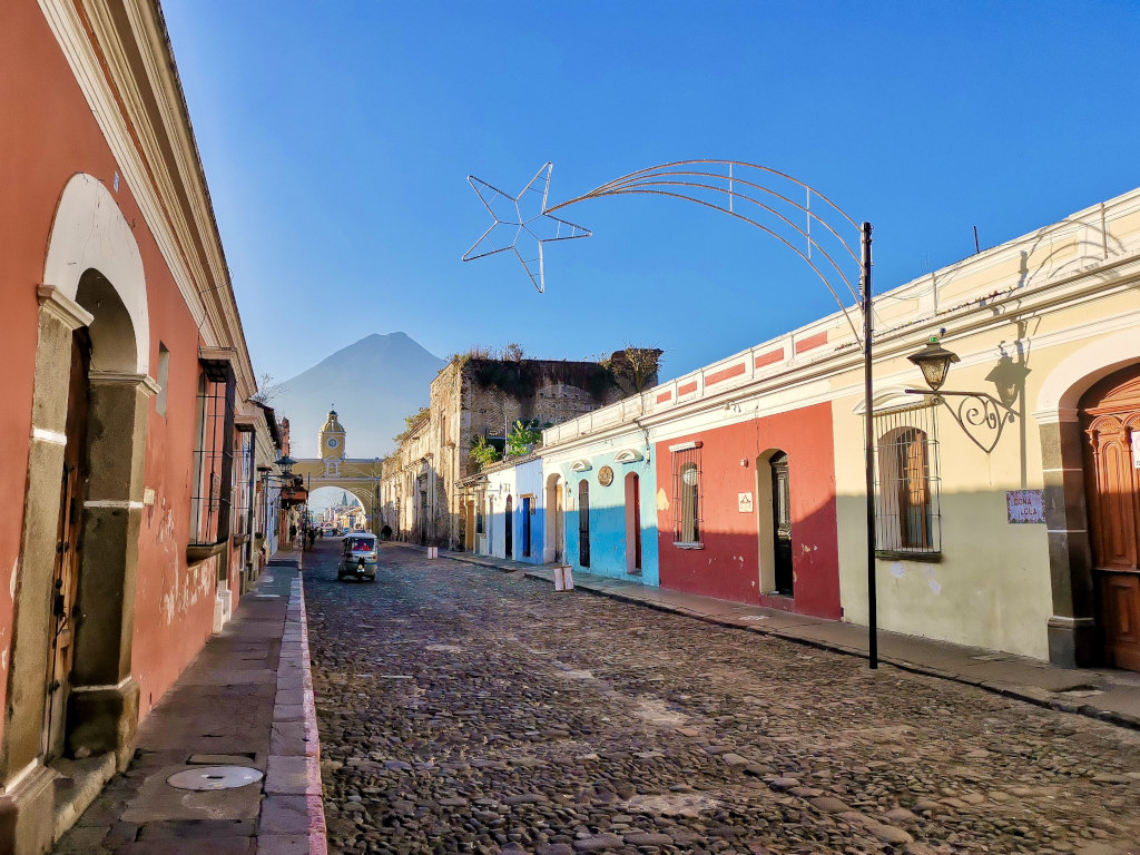 A tuk tuk driving down a cobble stone street with Christmas decoration in Antigua Guatemala