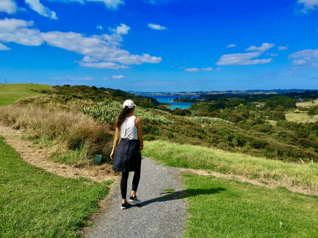 A woman in a white singlet and black leggins walking along a gravel travel at the entrance to the Mangemangeroa Reserve walkway