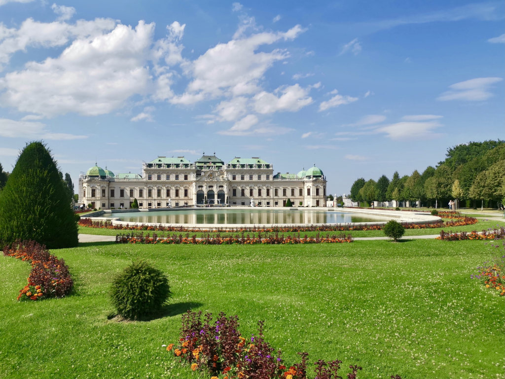 A pool of water surrounded by flowers in front of a building at belvedere palace