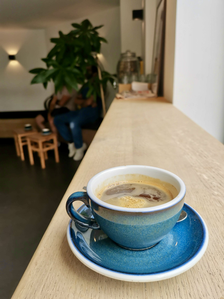 A blue ceramic cup of coffee sitting on a wooden bench at Five Ways Coffee Roasters, one of the best cafes in Amsterdam.