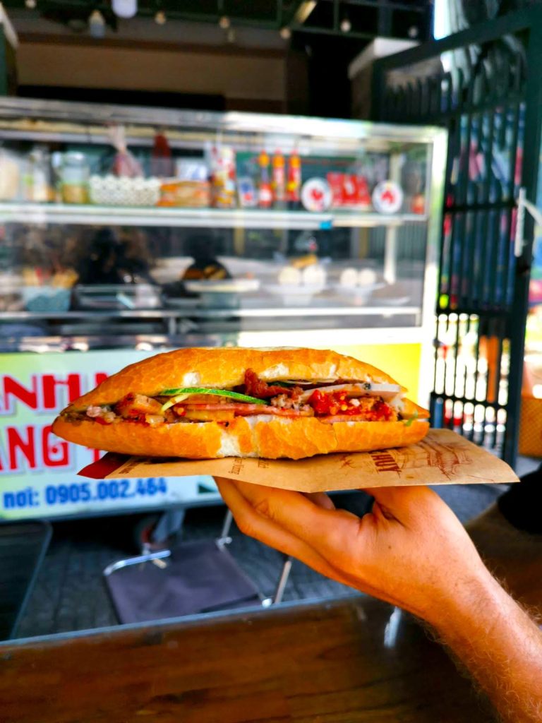 Crispy Vietnamese Banh Mi sandwich held in hand, showing fresh vegetables and chili, representing the cheap and delicious food for digital nomads in Hoi An.