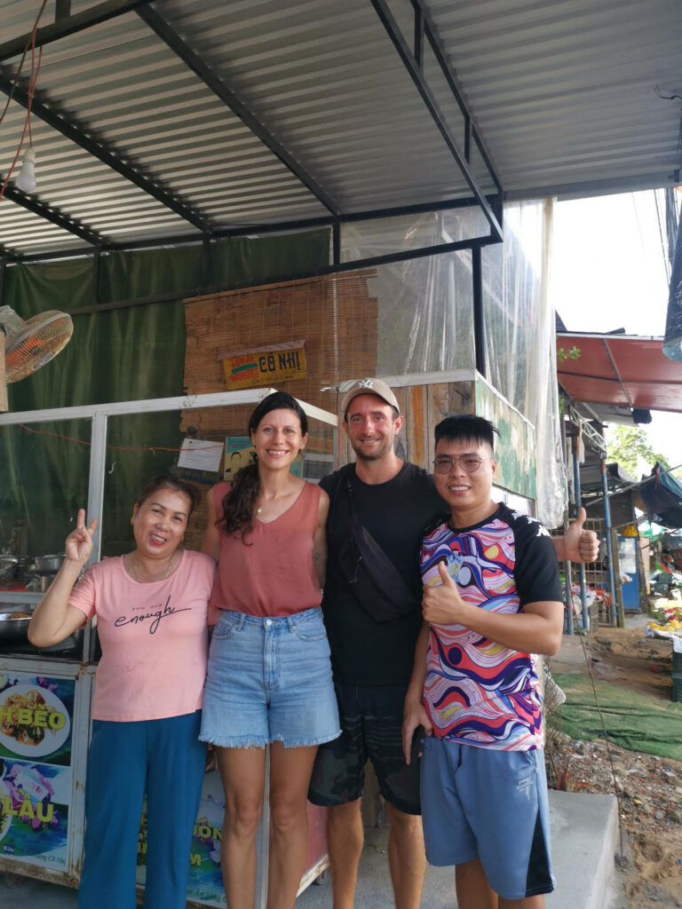 Allan and Katharina standing with their arms around the owners of a street food stall in hoi an vietnam with smiles on their faces