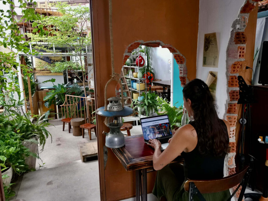 Katharina sitting at a laptop in a cafe at a desk that looks through a hole in a brick wall in Da Nang