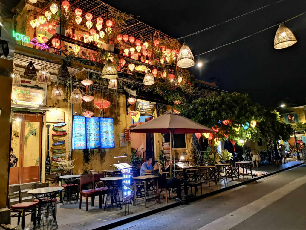Restaurant storefront in Hoi An at night, decorated with dozens of lit, colorful paper lanterns and wicker baskets, showing the town's magical atmosphere as a popular day trip from Da Nang.