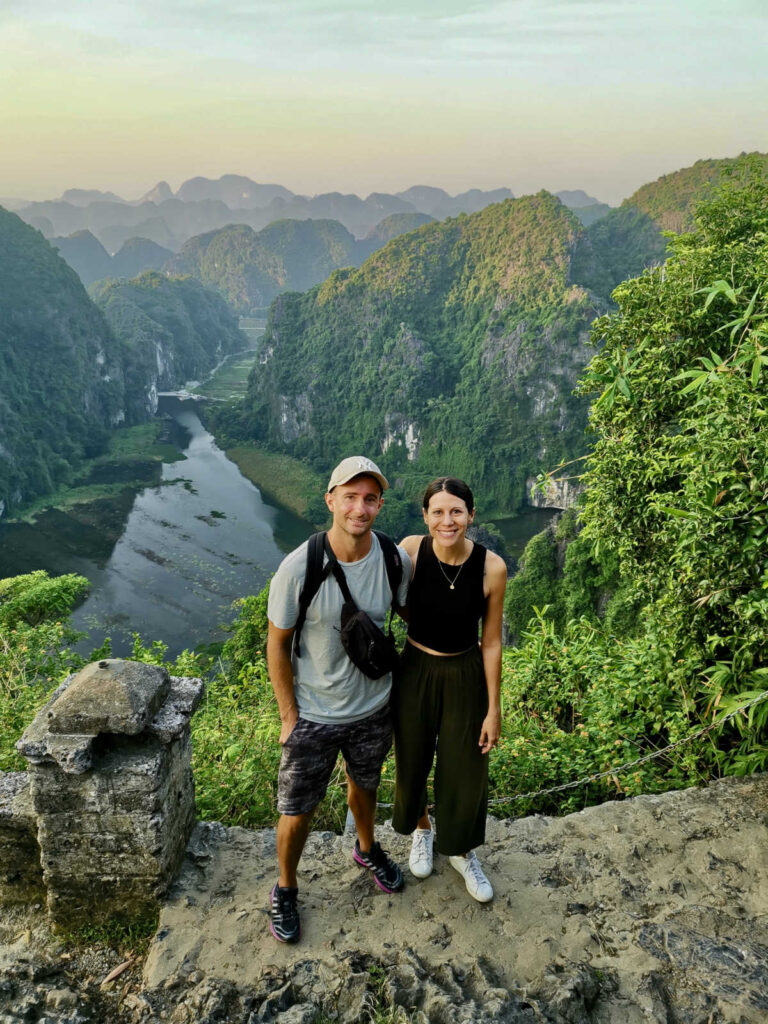 Allan and Katharina standing with there arms around each other with a spectacular view of the limestone karst cliffs of Ninh Binh in the background at sunset