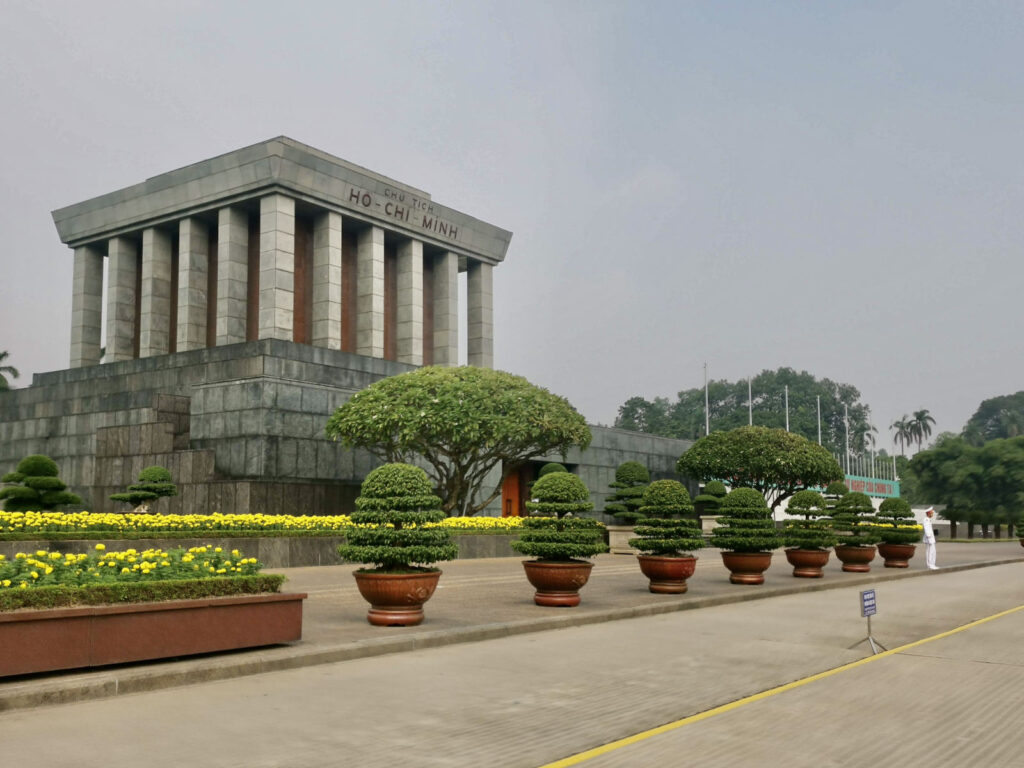 The Ho Chi Minh Mausoleum is a prominent landmark in Hanoi, Vietnam, featuring a grand, stone structure surrounded by manicured gardens and potted bonsai trees.