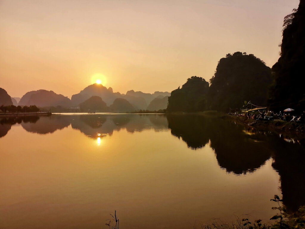 The sun setting over a lake with reflections of the surrounding karst mountains, a bar area is visible on the right side of the photo.