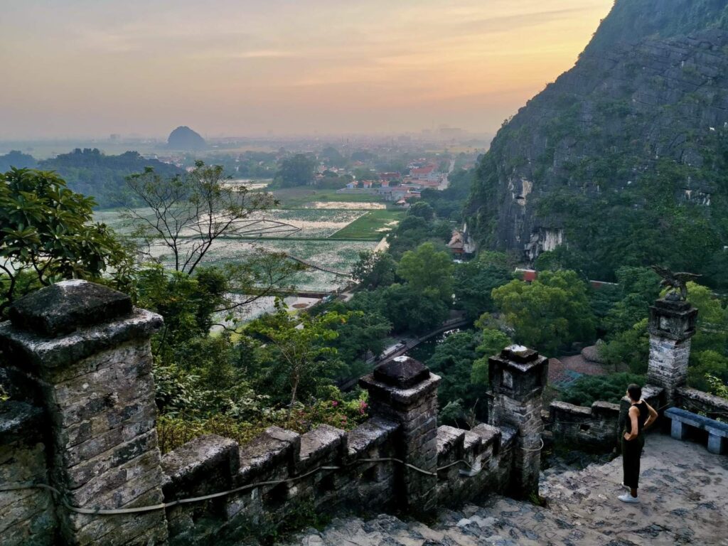 A traveler in dark green pants and a black top climbing the white stone stairs of Mua Cave at dawn to beat the crowds and heat.