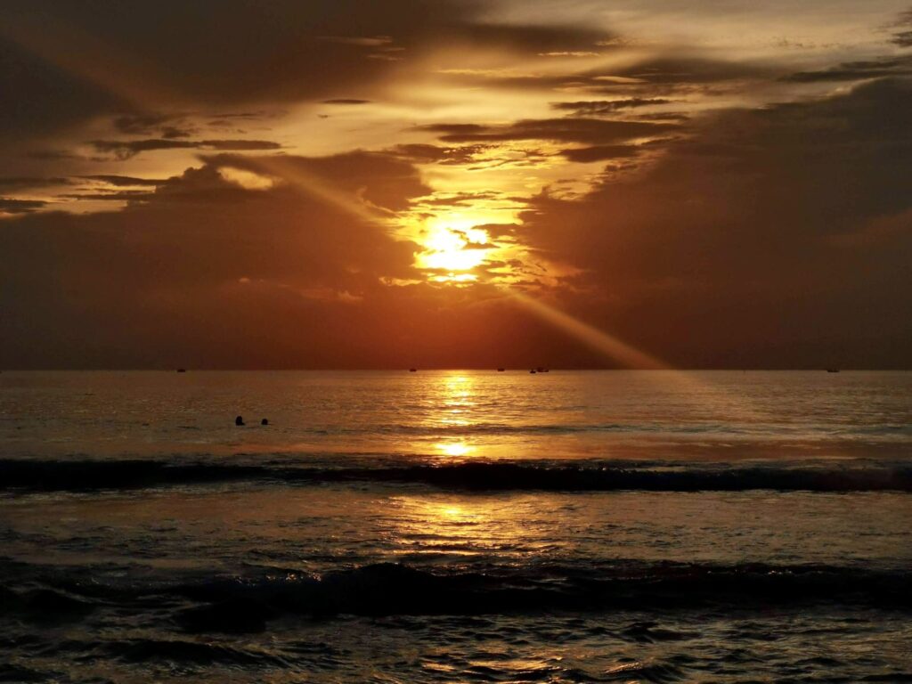 Dramatic orange and gold sunrise over the ocean waves at Da Nang beach, with sun rays breaking through the clouds.