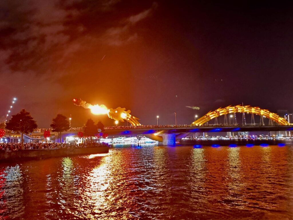 The Dragon Bridge in Da Nang illuminated at night, showing the large yellow dragon structure spanning the Han River, a symbol of the city's modern architecture.