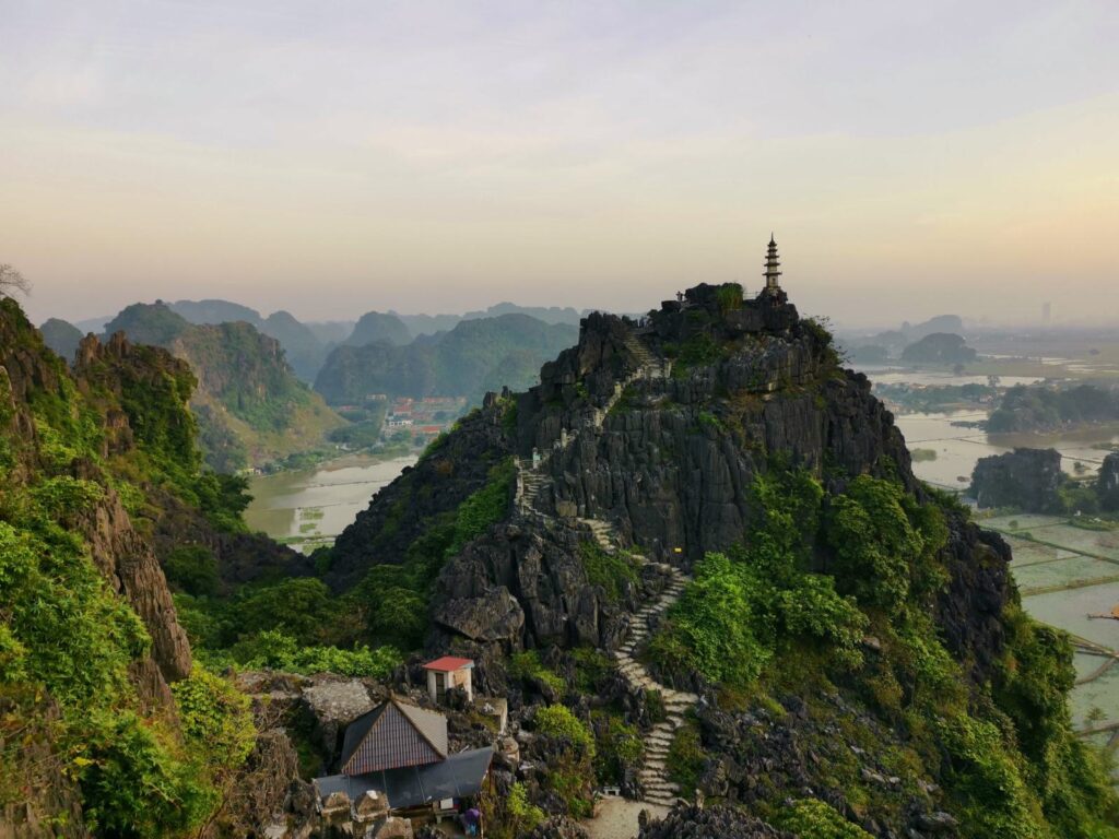A wide landscape view of the steep stone staircase winding up the limestone mountain to the pagoda at the peak of Mua Cave lookout in Ninh Binh.