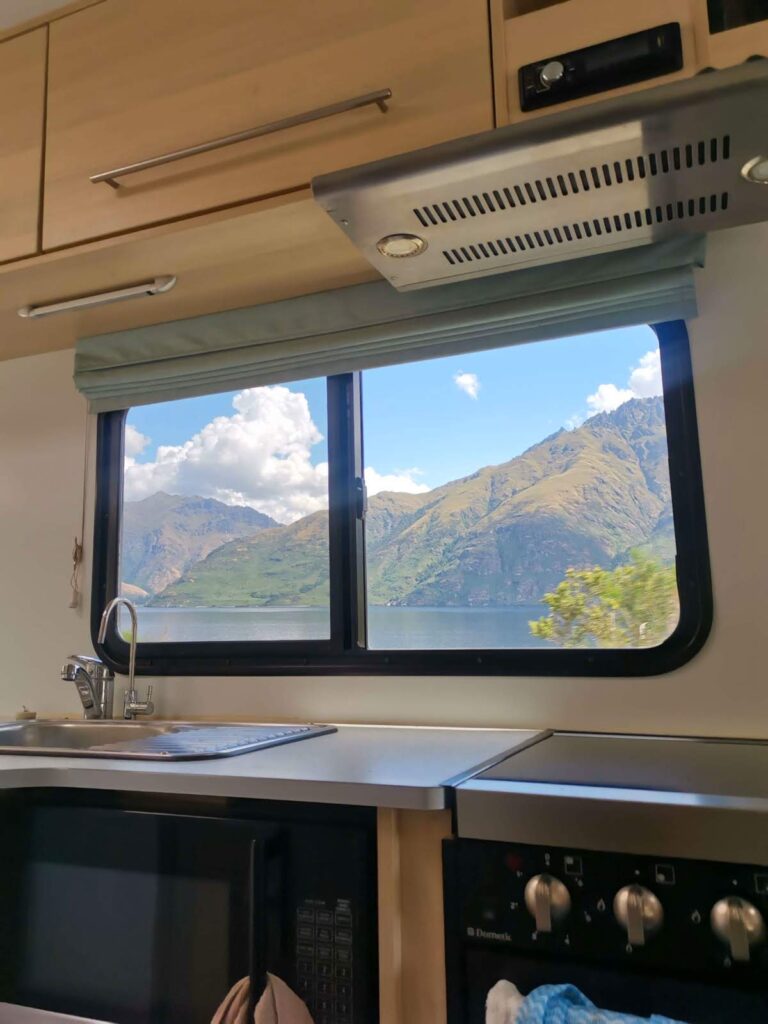 The view of mountains and a blue lake through the kitchen window of a campervan in New Zealand.