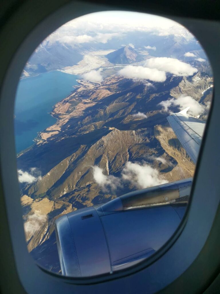 An aerial view looking out of a plane window over the Southern Alps and a bright blue lake near Queenstown.