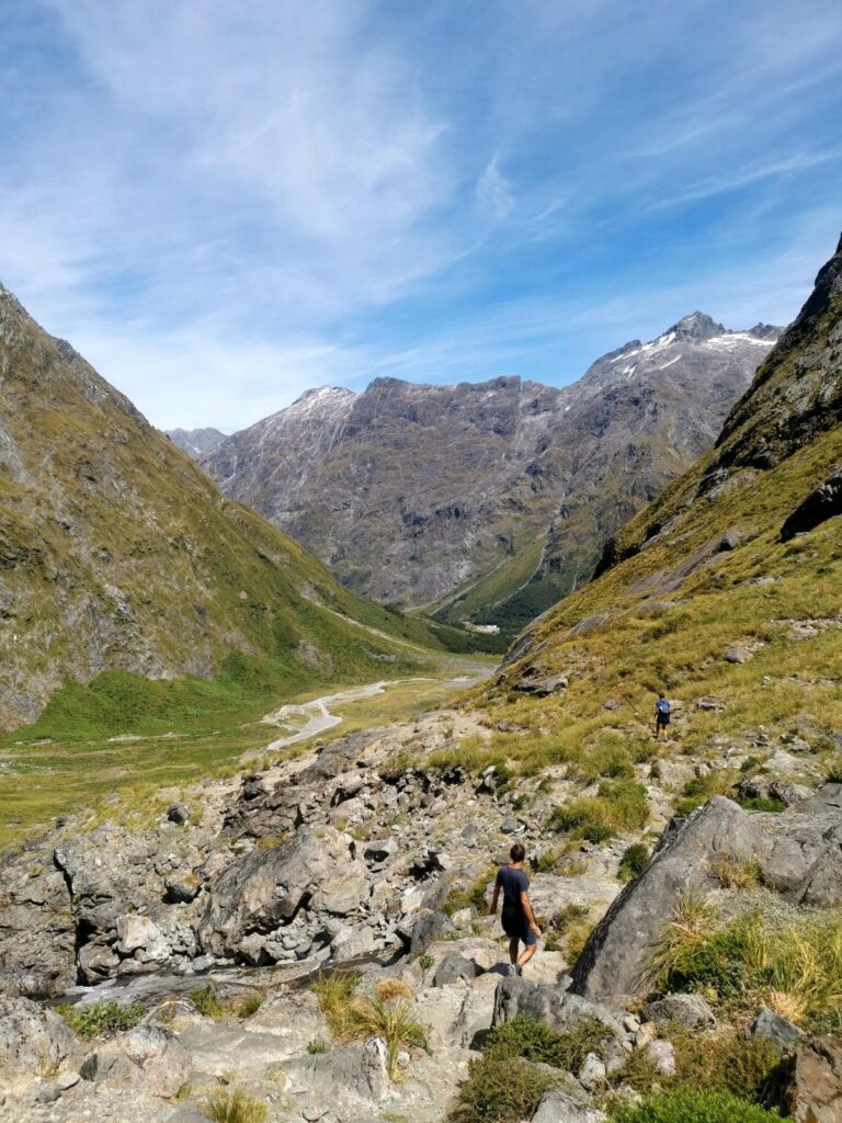 Hikers descending a rocky mountain trail of Gertrude Saddle into a wide green valley surrounded by steep granite peaks.