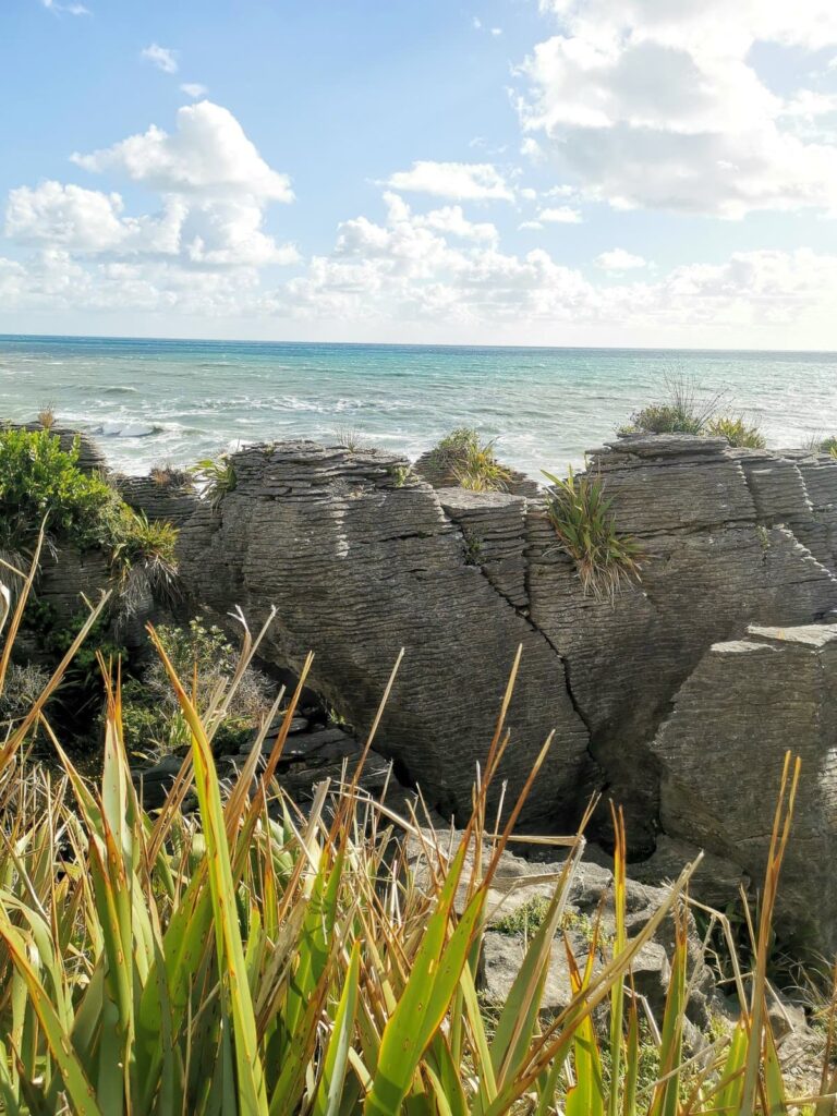 A view of the unique limestone formations of the Pancake Rocks in Punakaiki, with the blue Tasman Sea and a cloudy sky in the background.
