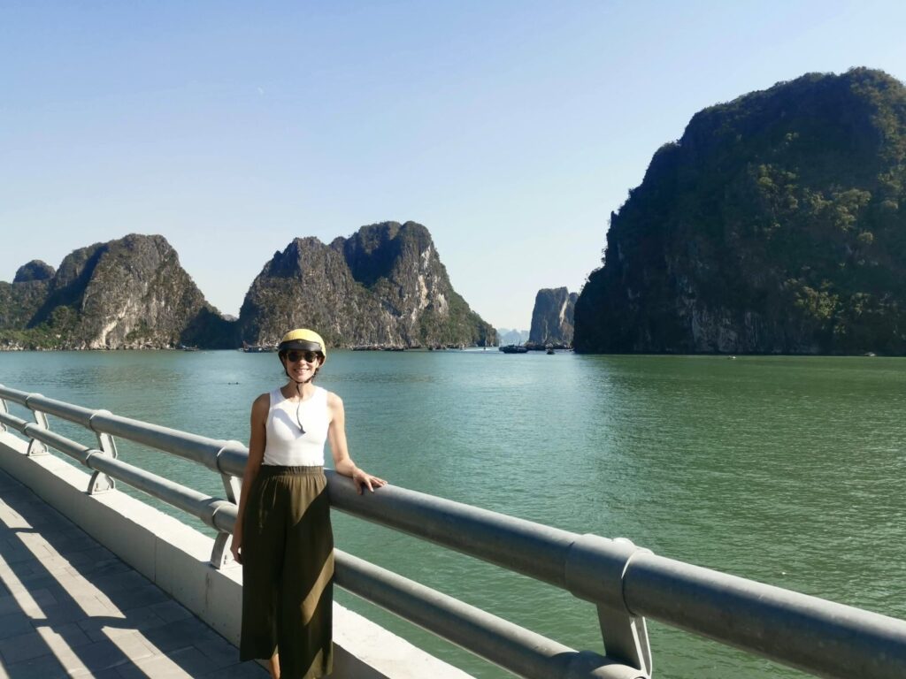 Katharina standing by the water with limestone cliffs and emerald water in Ha Long Bay Vietnam