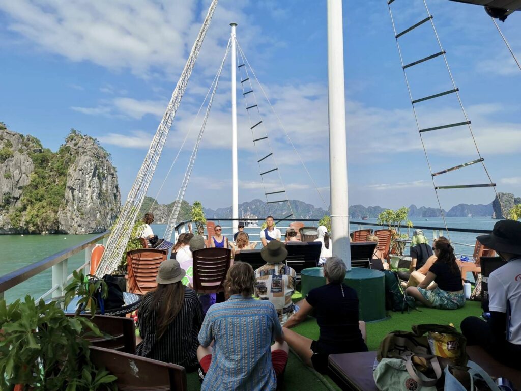 Travelers relaxing on the deck of a cruise boat in Ha Long Bay surrounded by limestone islands