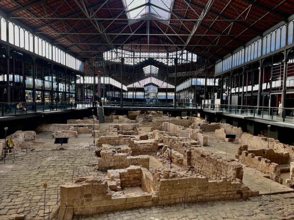Wide elevated view of excavated 18th-century stone street and house ruins beneath the iron roof of El Born Cultural Center in Barcelona.