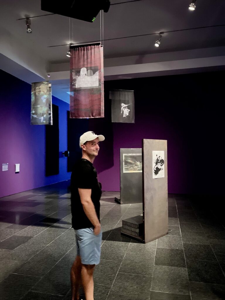 Allan standing inside a dark purple gallery room surrounded by suspended artwork at MACBA in Barcelona
