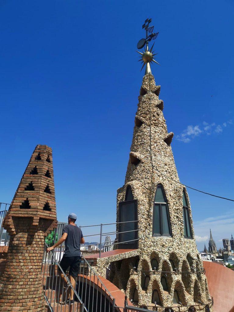 Allan walking up stairs on the rooftop of Palau Güell next to unique mosaic-tiled chimneys in Barcelona.