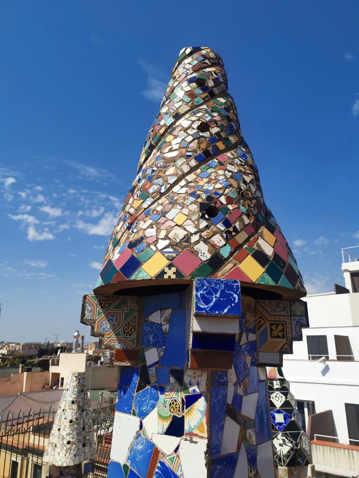 A close-up of a colorful, trencadís ceramic mosaic chimney on the rooftop of Palau Güell against a blue sky in Barcelona.