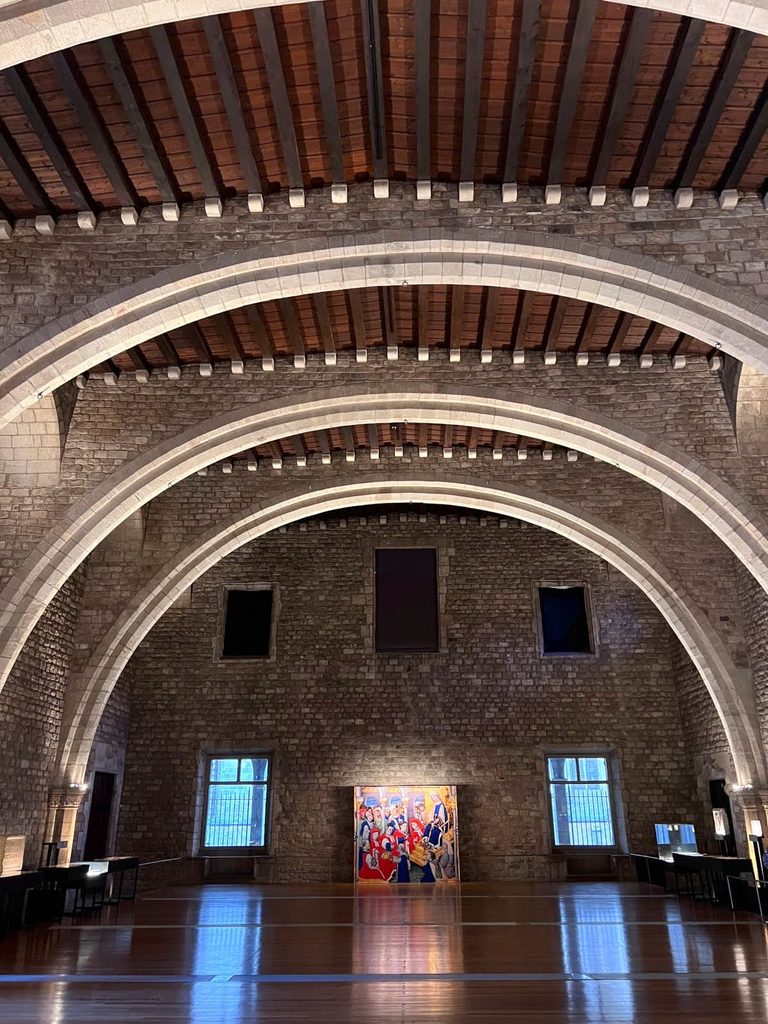 The grand medieval stone arches and wooden ceiling inside the Saló del Tinell hall at MUHBA Museu d'Història de Barcelona.